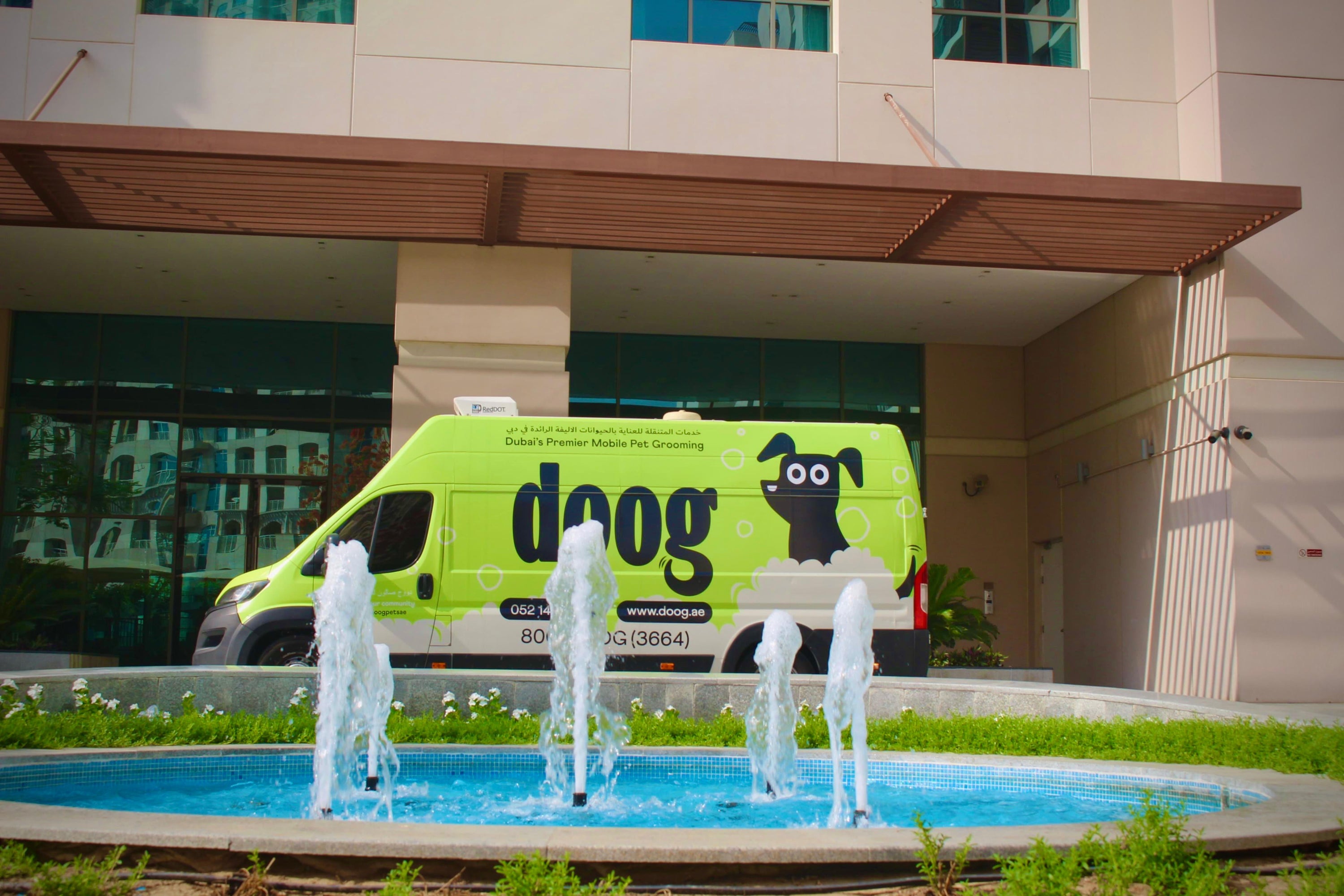 A Doog mobile grooming van parked next to beautiful fountains, showcasing the convenience of on-site pet grooming in a scenic outdoor location.